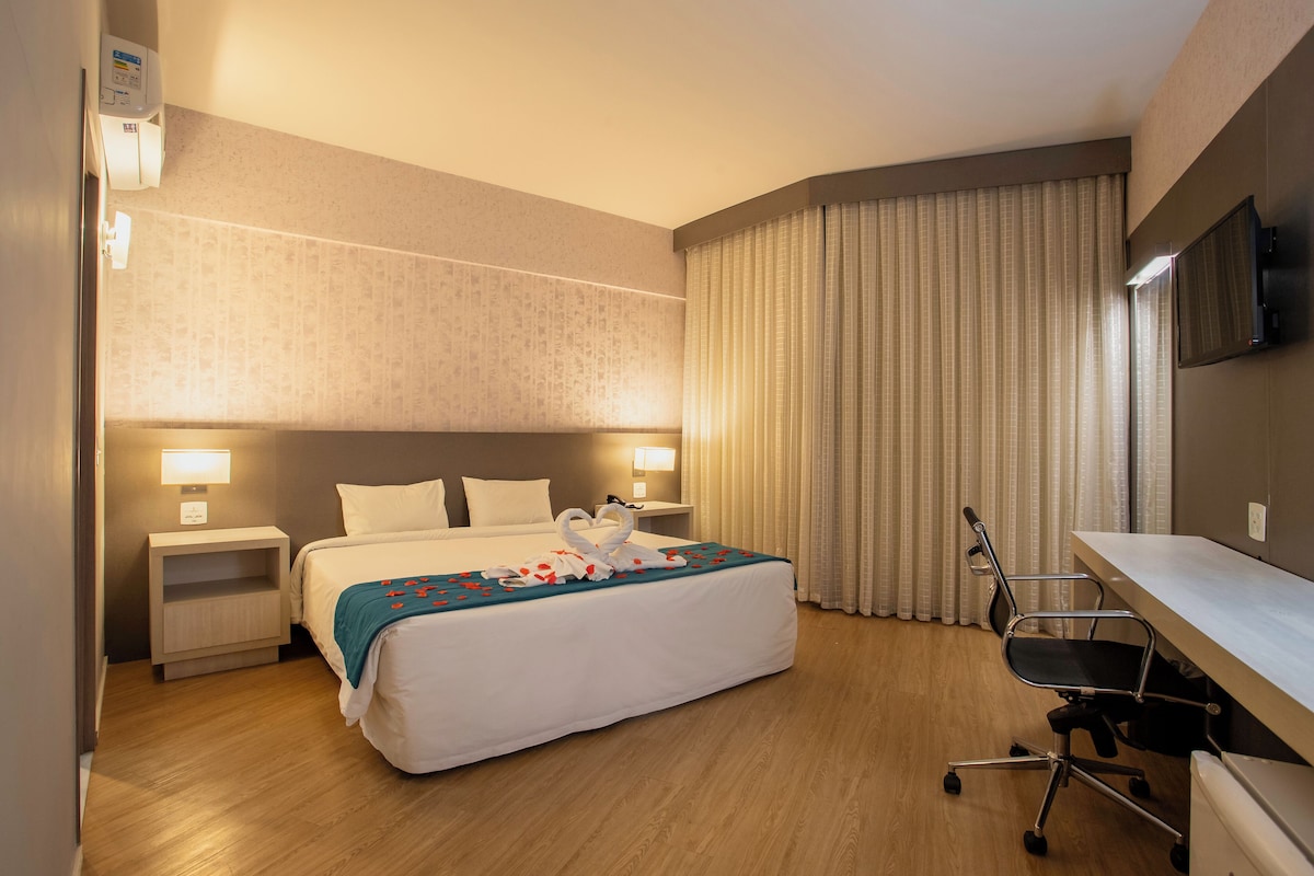 Habitación de hotel con una cama grande, mesitas de noche con lámparas, un escritorio con silla y un televisor montado en la pared.