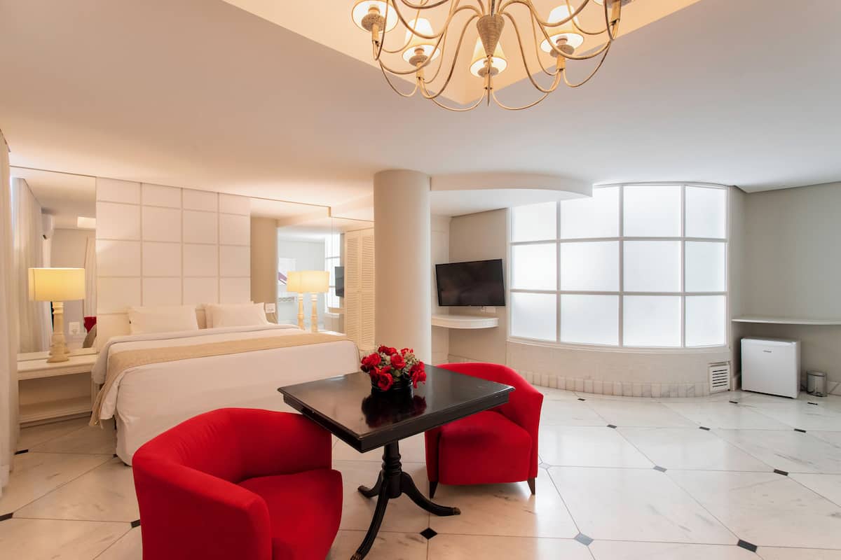 Een moderne hotelkamer met een bed, een televisie, een tafel met een bloemenvaas en rode stoelen.