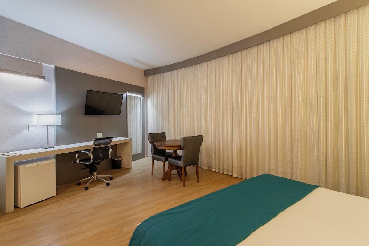 Een hotelkamer met een bed, bureau, stoel en een televisie aan de muur.