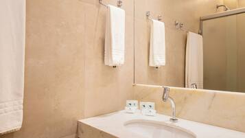 A modern bathroom with a marble sink, multiple towel hooks, and a large mirror.