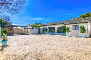A courtyard with a paved ground, potted plants, and a building with a tiled roof. - BM Gardens Apartment Hotel (Germiston)