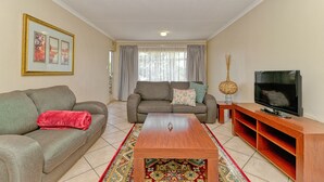 A living room with a sofa, a coffee table, a TV, and a decorative vase. - BM Gardens Apartment Hotel (Germiston)