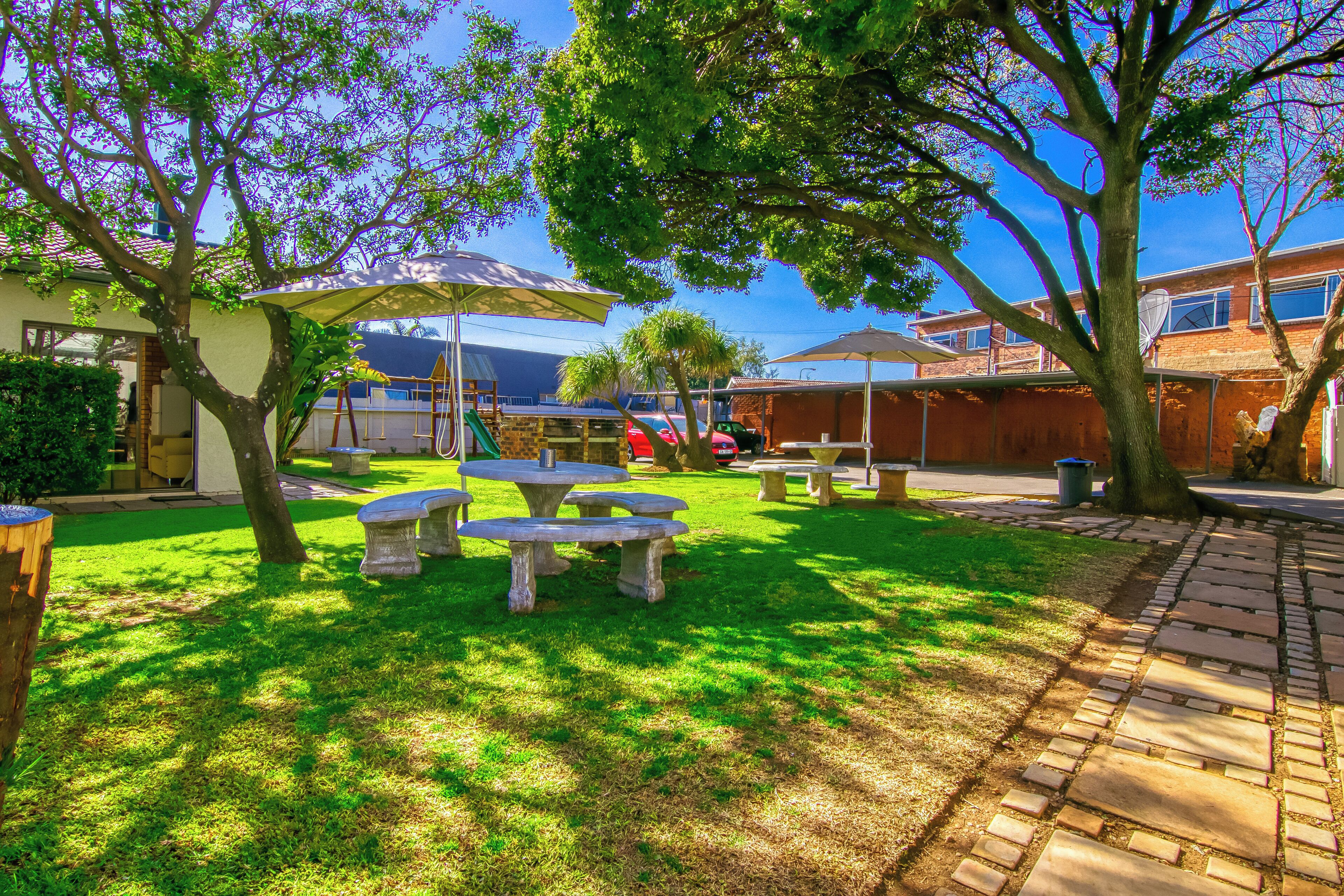 A backyard with a picnic table and umbrella, surrounded by trees and a brick pathway.