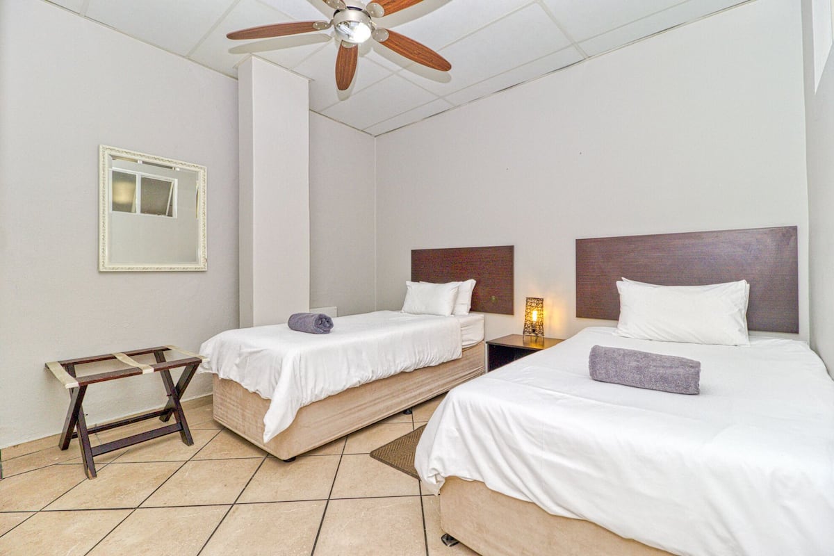 A hotel room with two beds, a ceiling fan, a bedside table with a lamp, and a framed picture on the wall.