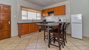 A kitchen with wooden cabinets, a black countertop, a sink, a stove, and a refrigerator. - BM Gardens Apartment Hotel (Germiston)