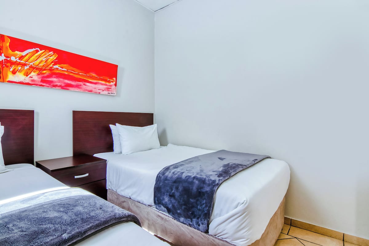 A hotel room with two beds, a nightstand, a wooden headboard, and a large abstract painting on the wall.