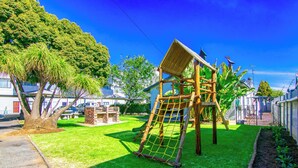 A playground with a climbing structure and a slide, surrounded by a well-maintained lawn and trees. - BM Gardens Apartment Hotel (Germiston)