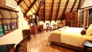 Een slaapkamer met een houten vloer, een bed met een witte dekbedovertrek, een bureau met een lamp en een kledingkast.