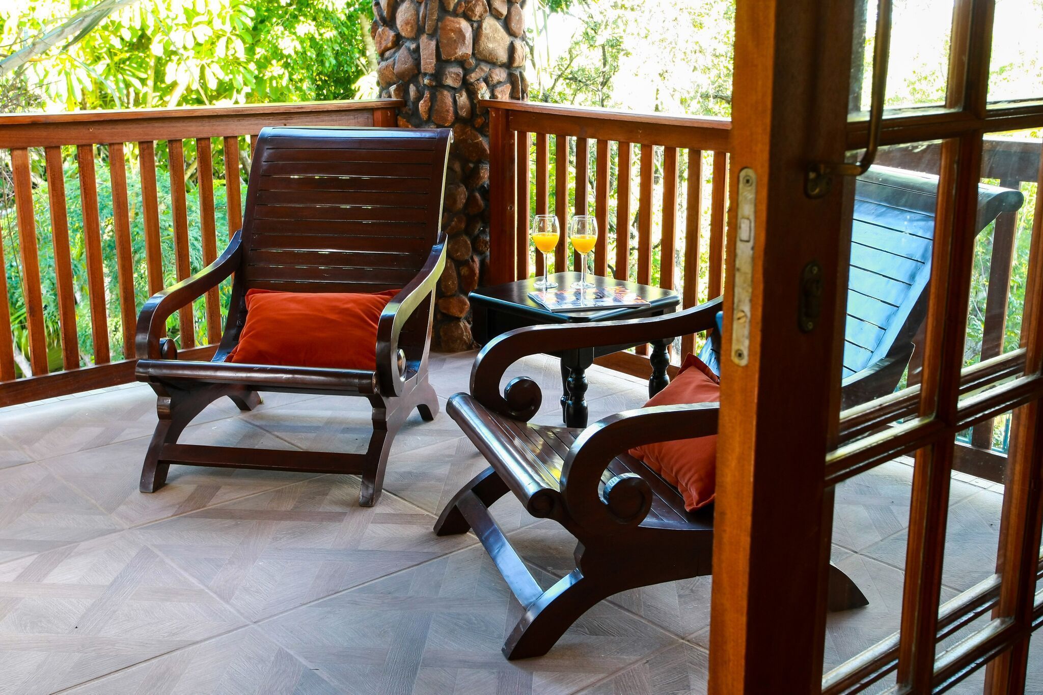 A wooden deck with two wooden chairs and a small table, surrounded by a stone pillar and a wooden railing.
