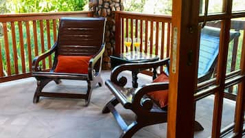 A wooden deck with two wooden chairs and a small table, surrounded by a stone pillar and a wooden railing.