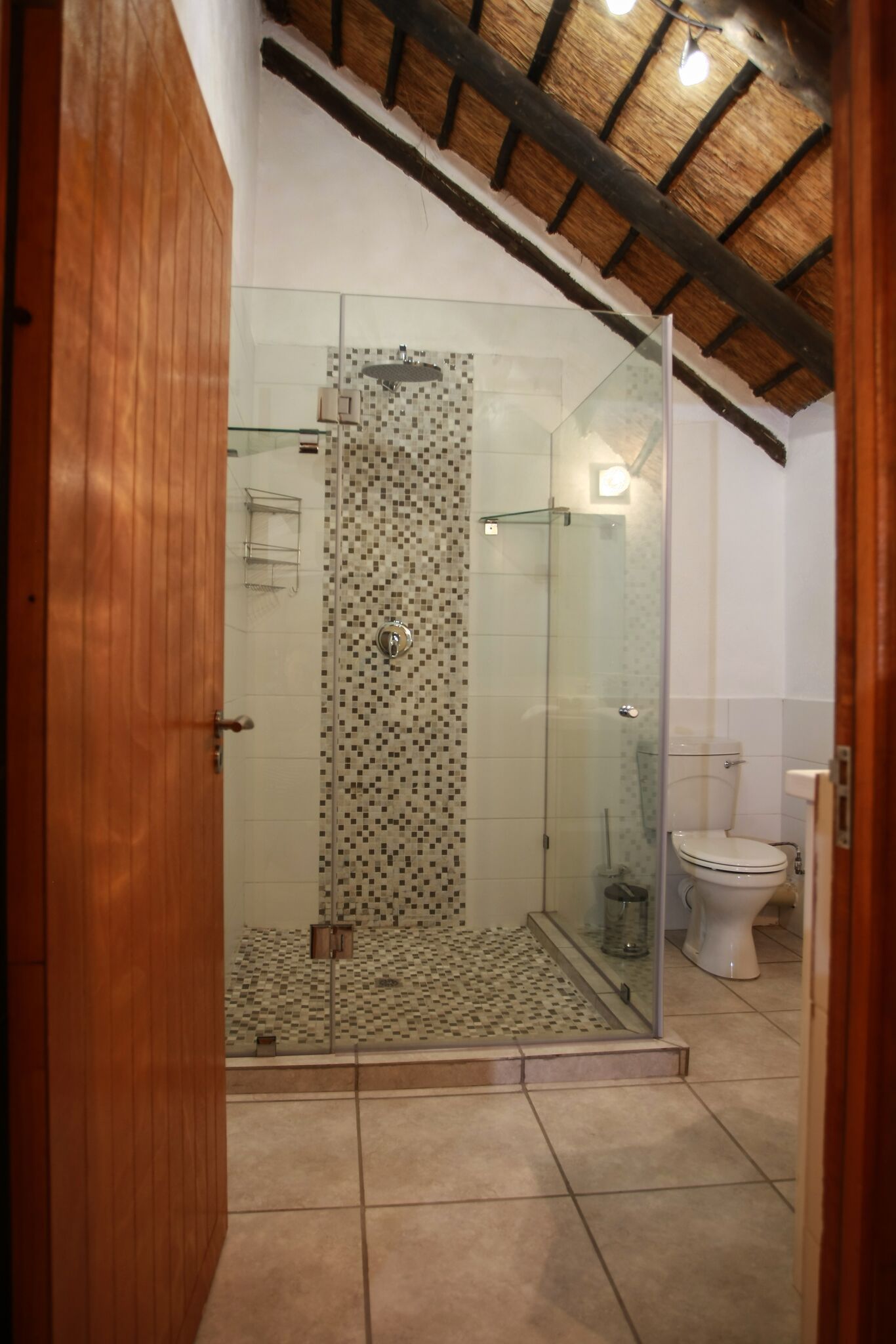 A bathroom with a glass-enclosed shower, a toilet, and a tiled floor.