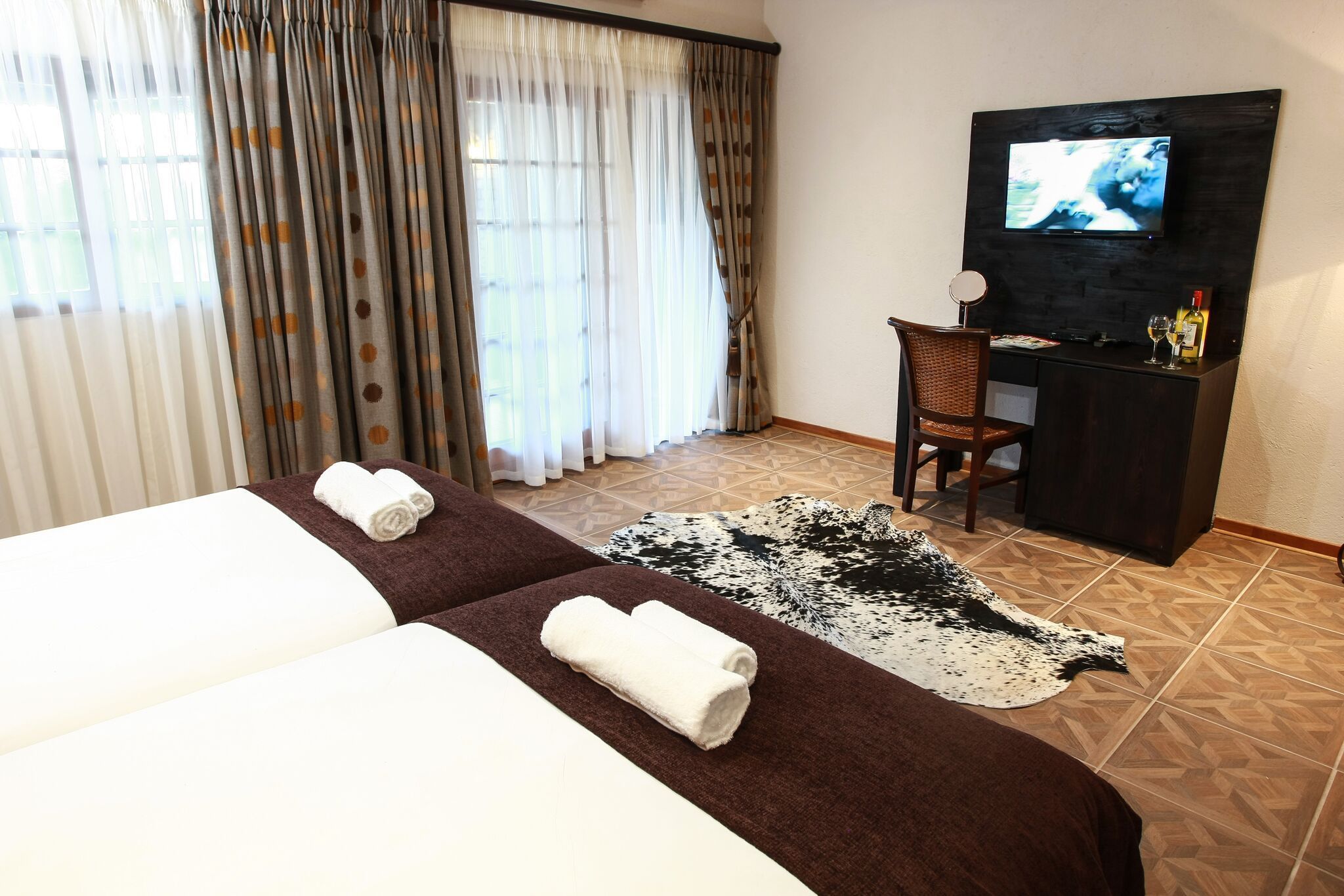 A hotel room with two beds, a TV, a desk with a chair, and a rug.