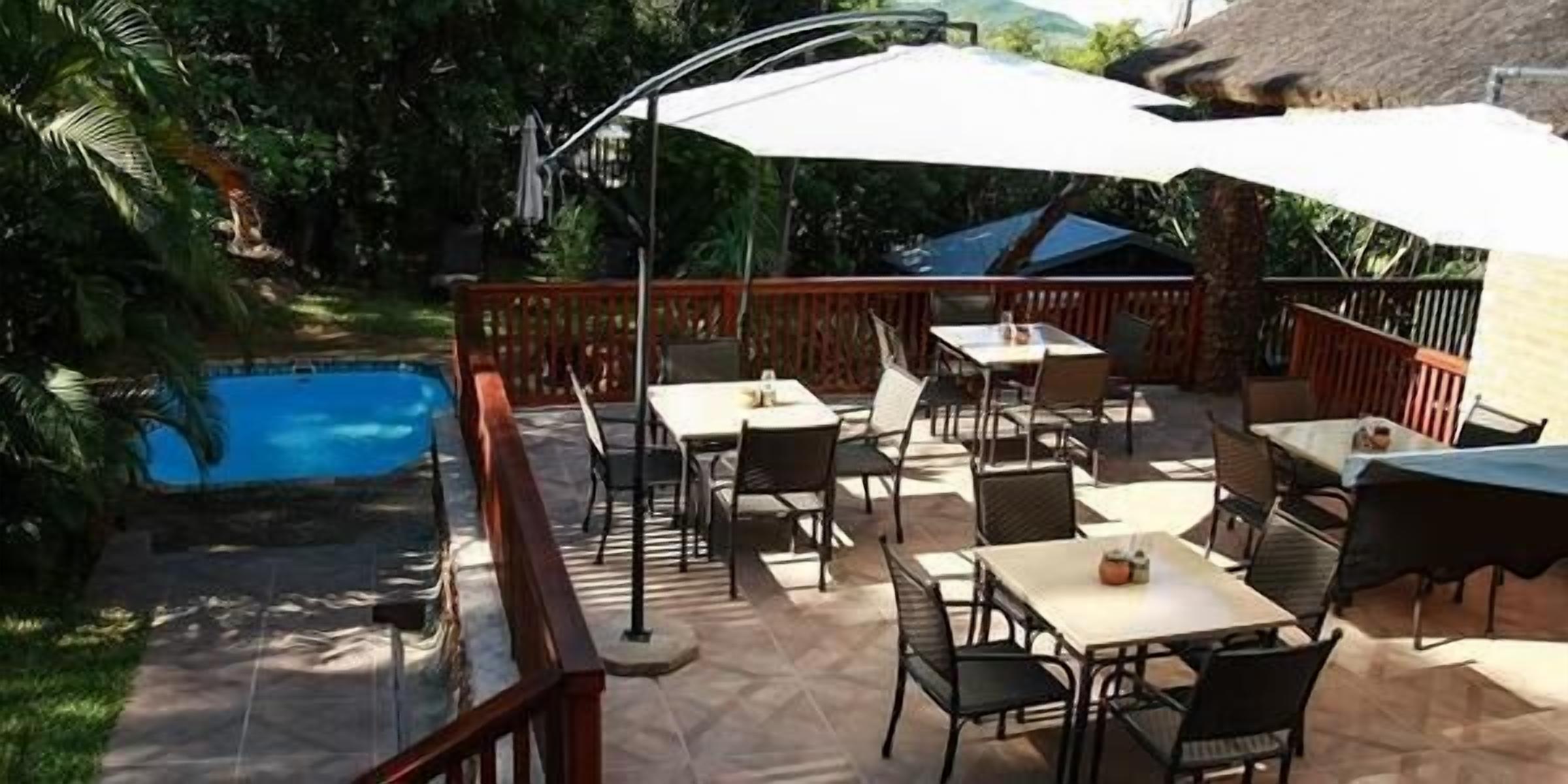An outdoor patio with tables and chairs, a pool, and a wooden fence.