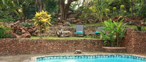 A swimming pool surrounded by a stone wall, with a chair and a table nearby.