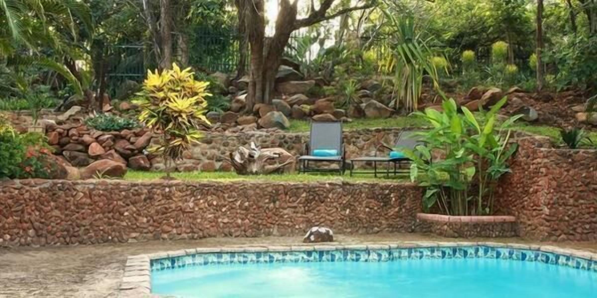 A pool surrounded by a stone wall, with a chair and a small table nearby.