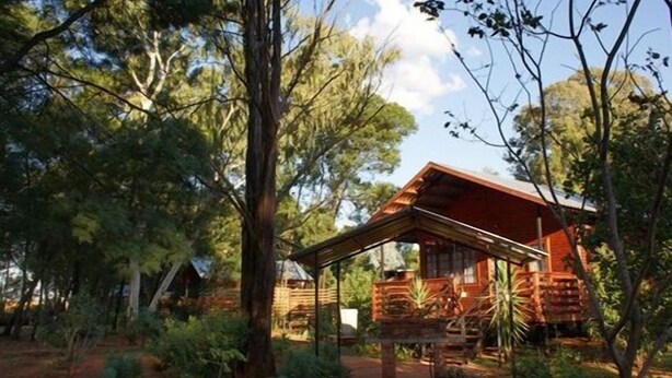 A rustic cabin with a wooden structure, surrounded by dense trees and vegetation. - Woodland Gardens (Magaliesberg)