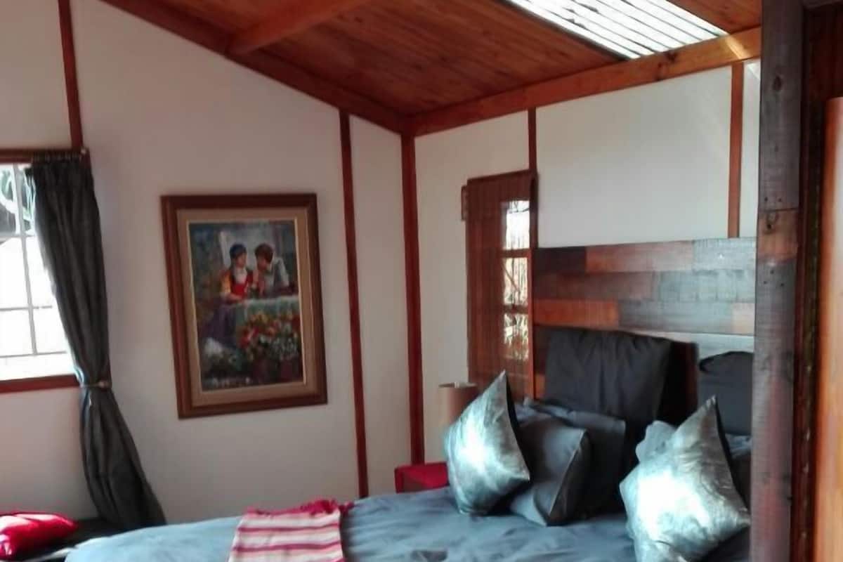 A bedroom with a bed, pillows, a blanket, a painting, and a window with curtains.