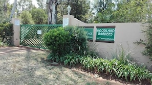 Une entrée fermée par un portail mène à une propriété appelée « Woodland Gardens », et un panneau indique la présence de chalets proposant un service de restauration autonome.