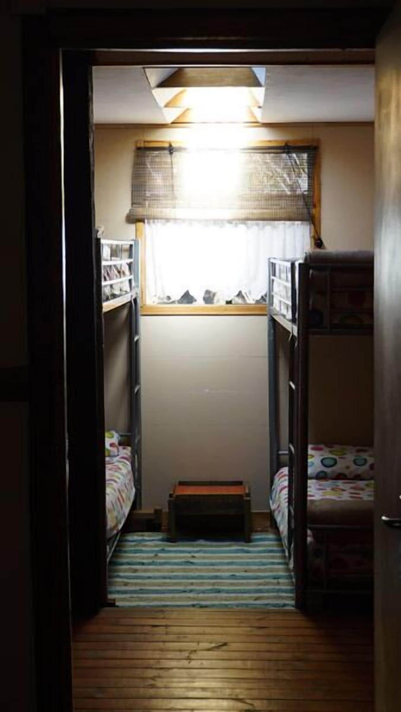 A narrow room with bunk beds, a small table, and a window with curtains.