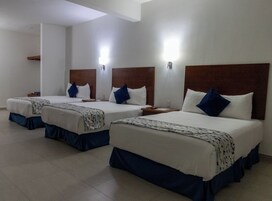 Habitación de hotel con tres camas, cada una con cabecero de madera y ropa de cama blanca.