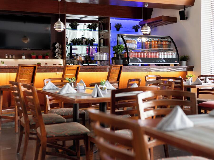 Een restaurant met houten tafels en stoelen, een bar met een displaykast en een televisie aan de muur.