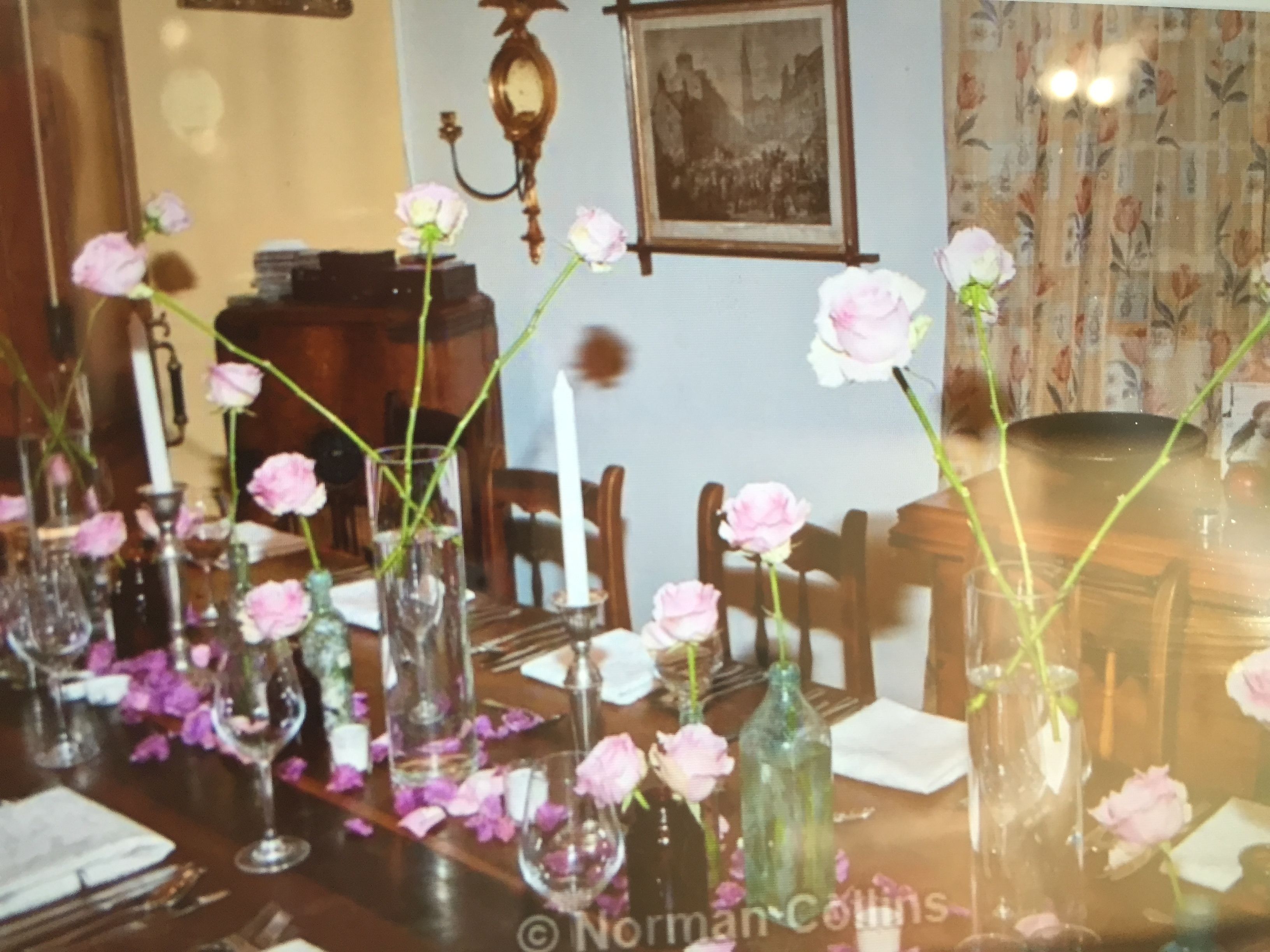 A dining table set with glass vases containing pink roses, surrounded by chairs and a candle holder.