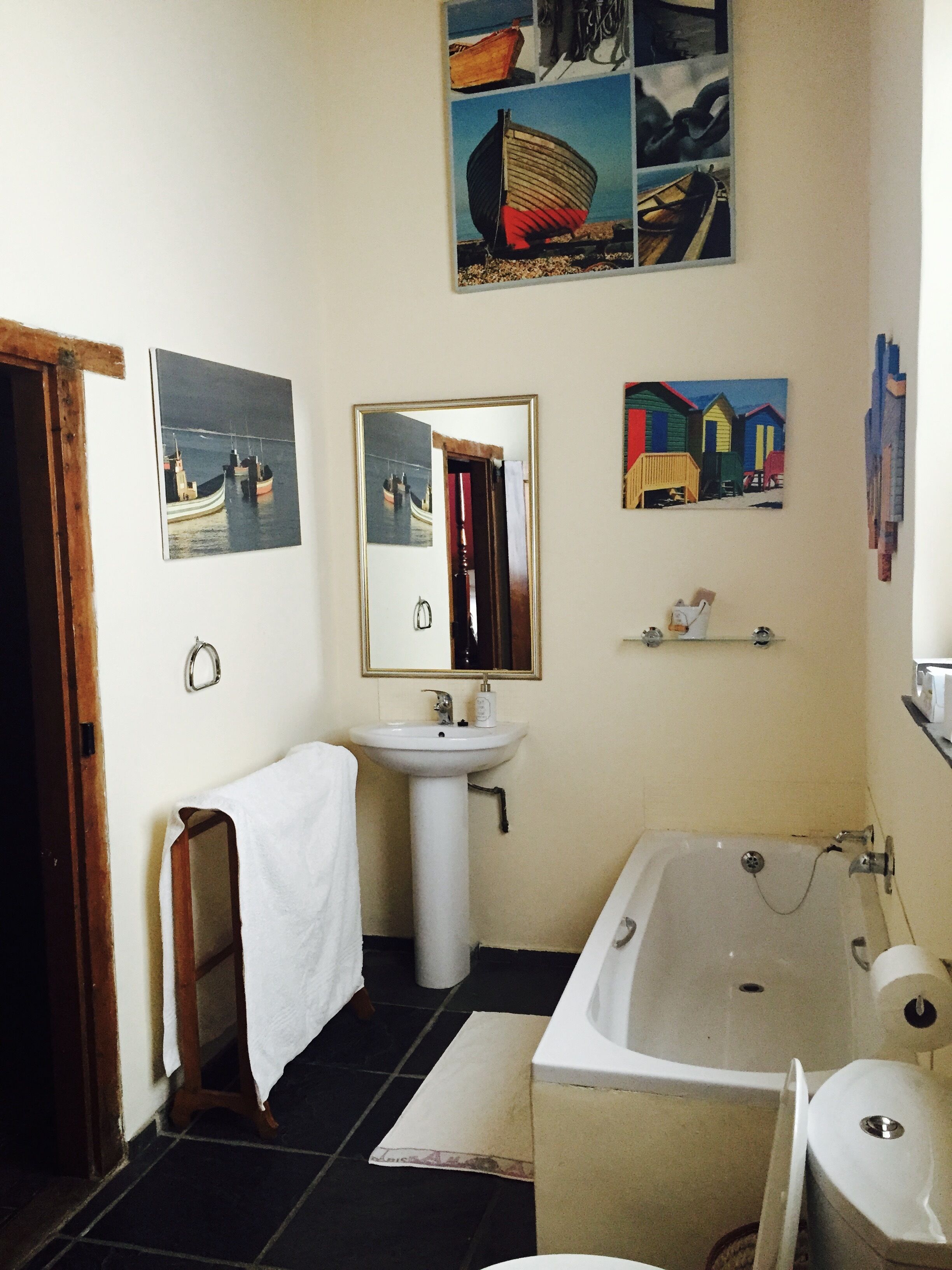 Une salle de bain avec une baignoire, un lavabo et un miroir. Il y a des tableaux au mur et une serviette est accrochée à la porte.