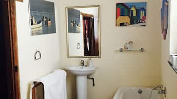 Une salle de bain avec une baignoire, un lavabo et un miroir. Il y a des tableaux au mur et une serviette est accrochée à la porte.