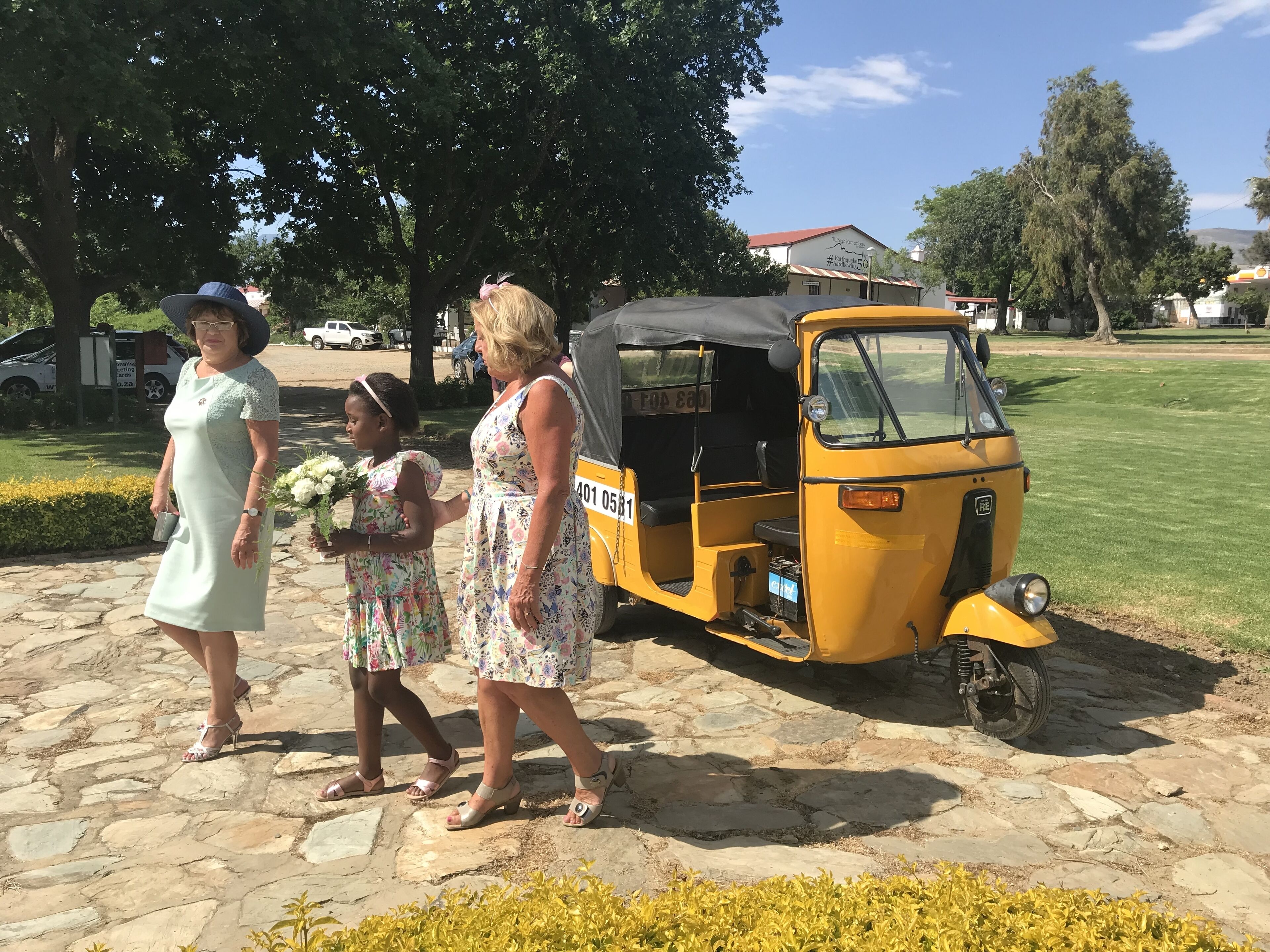 A stone-paved area with a yellow auto-rickshaw parked on the side.