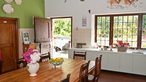 A dining area with a wooden table, chairs, a vase with flowers, and a bowl of fruit. - Wittedrift Manor House (Tulbagh)