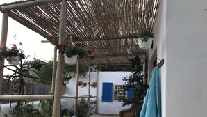 A covered outdoor area with hanging planters, a concrete floor, a wicker chair, and a blue shuttered window. - Wittedrift Manor House (Tulbagh)