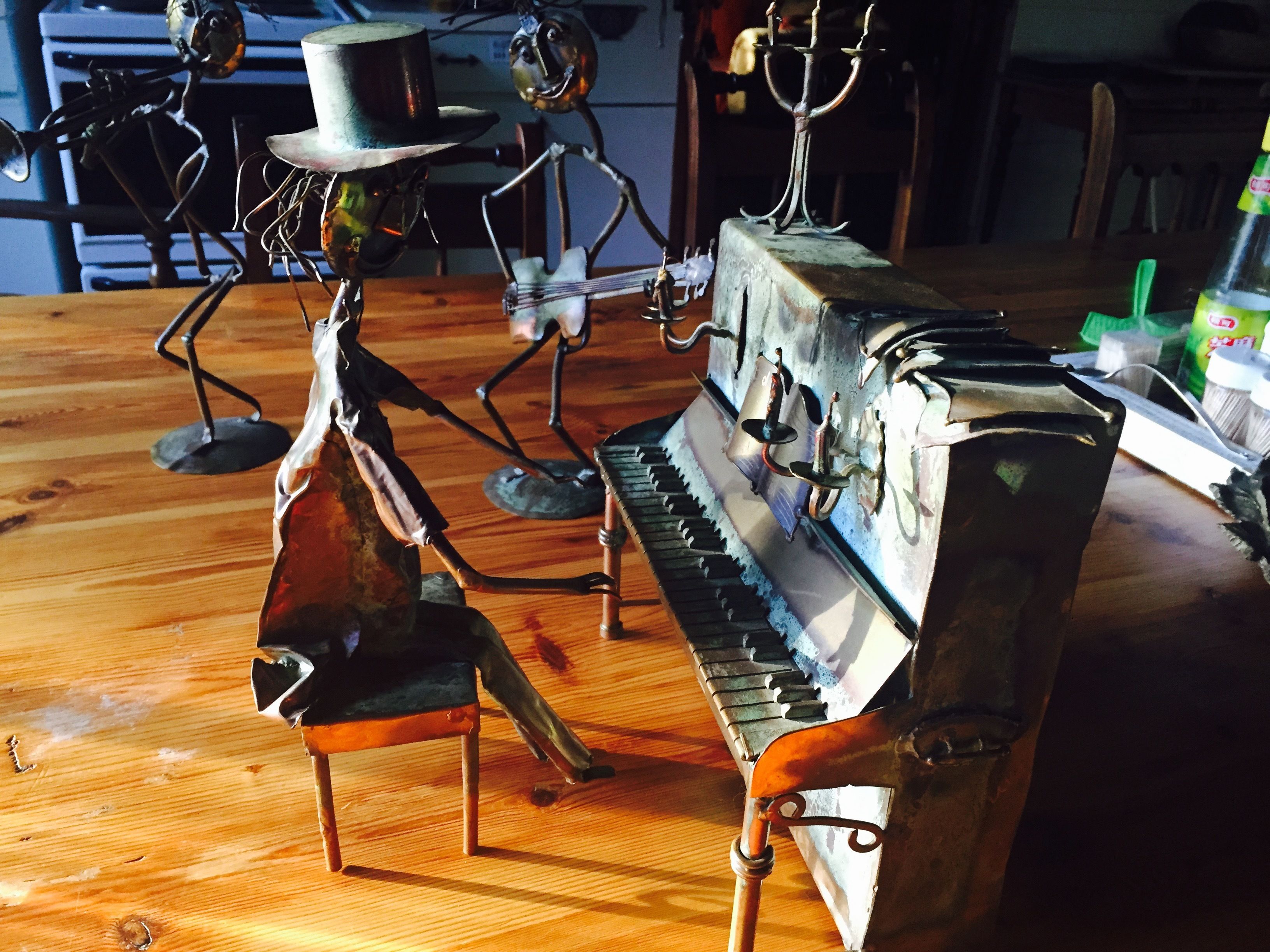 A piano with metal sculptures resembling animals and a hat on top.