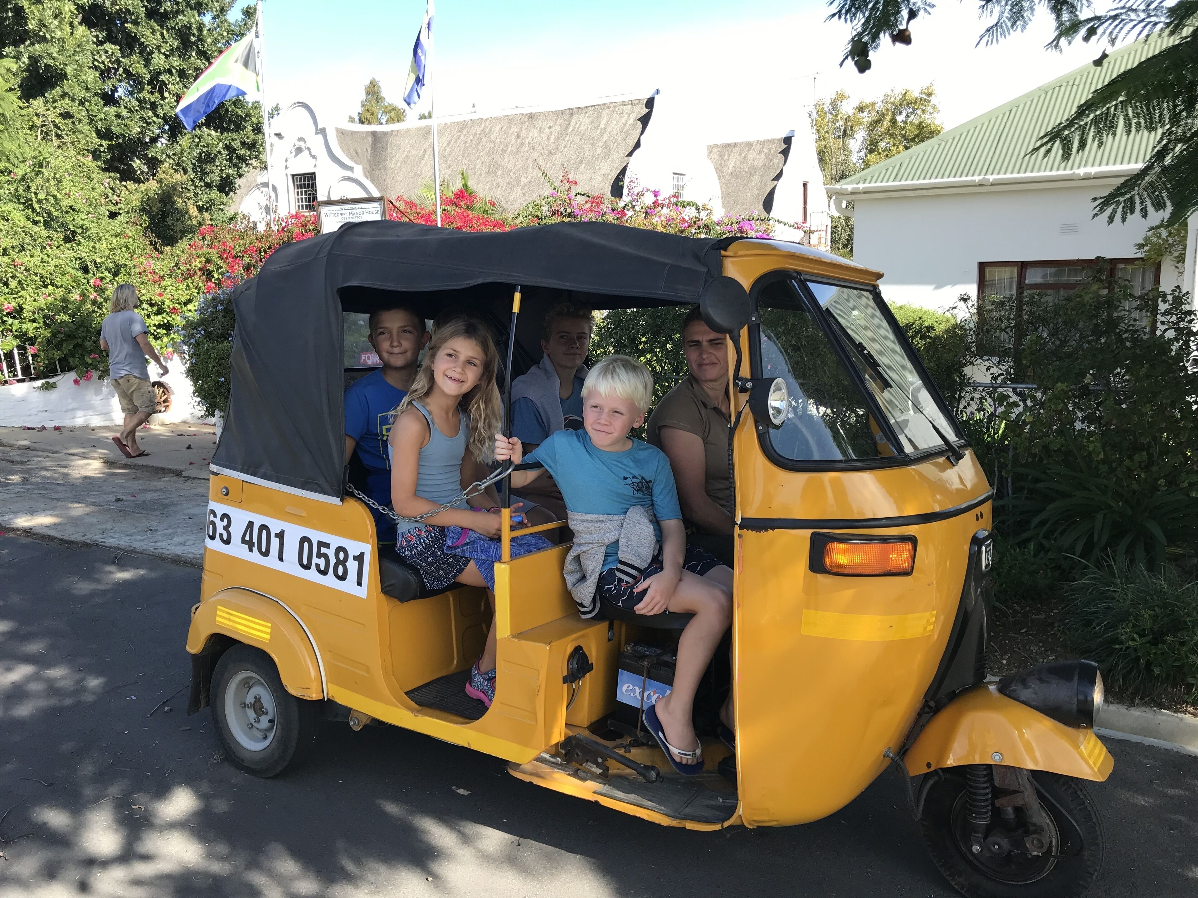 Een gele tuktuk met passagiers, geparkeerd op een straat met een gebouw op de achtergrond.