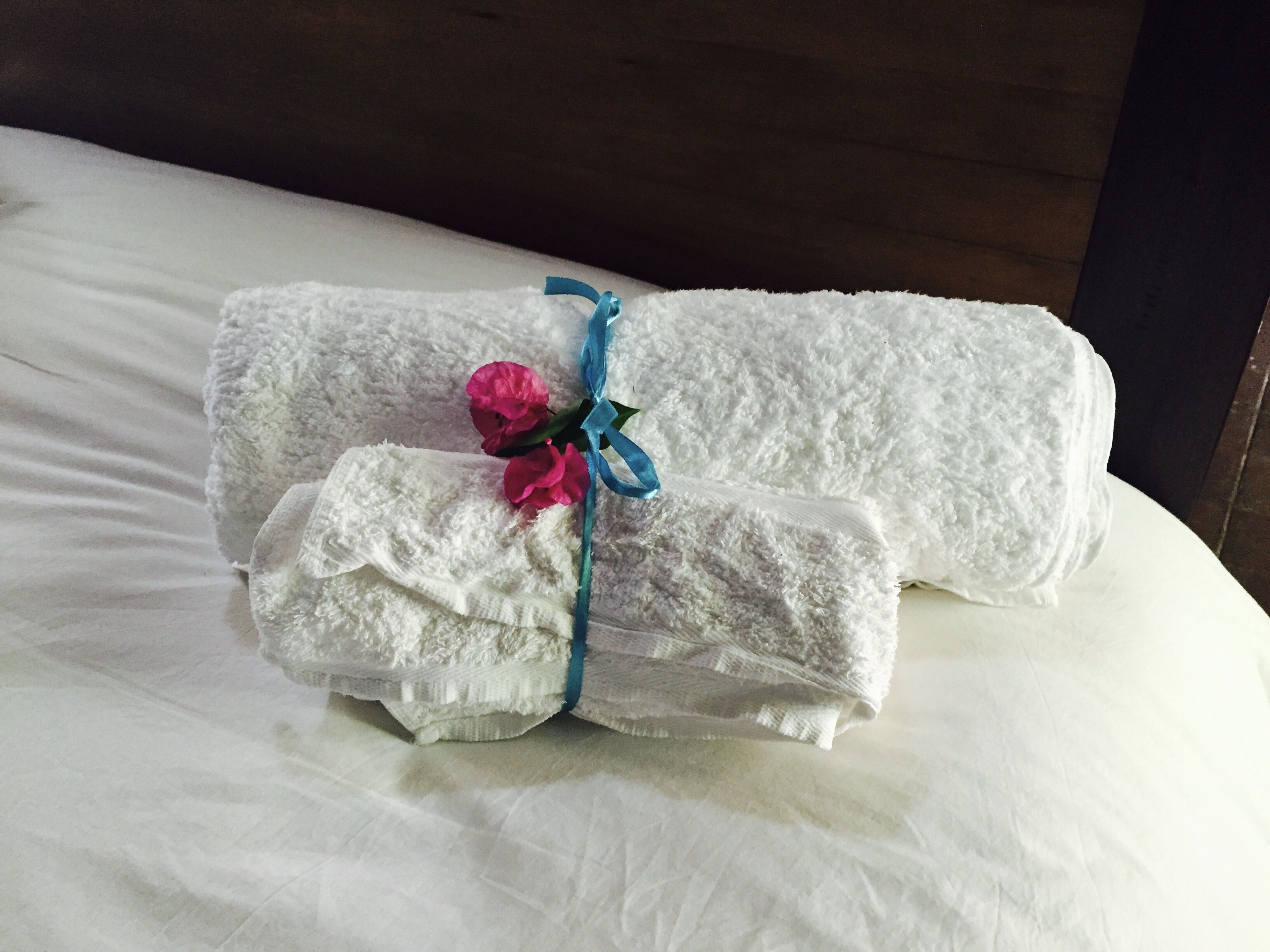 A neatly folded white towel with a blue ribbon and pink flowers on a bed.