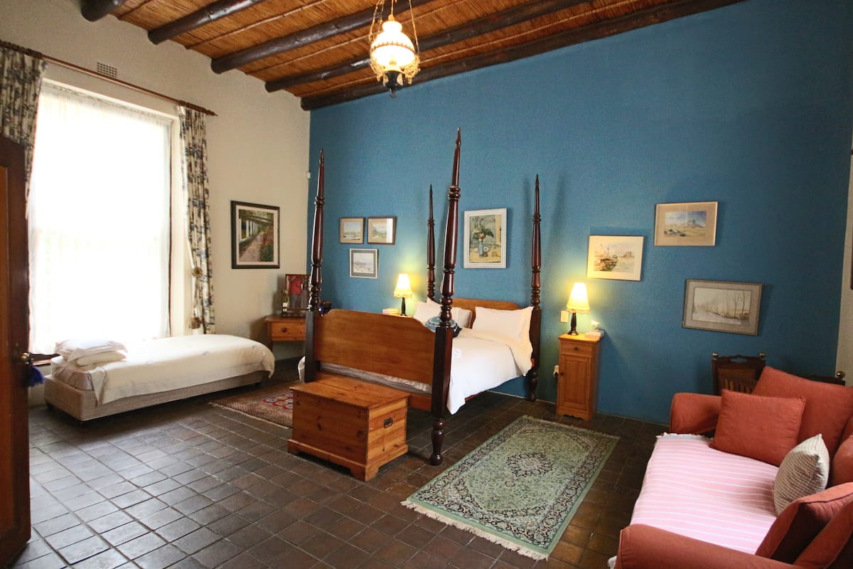 A bedroom with a four-poster bed, a single bed, a wooden nightstand, a red sofa, and a patterned rug.