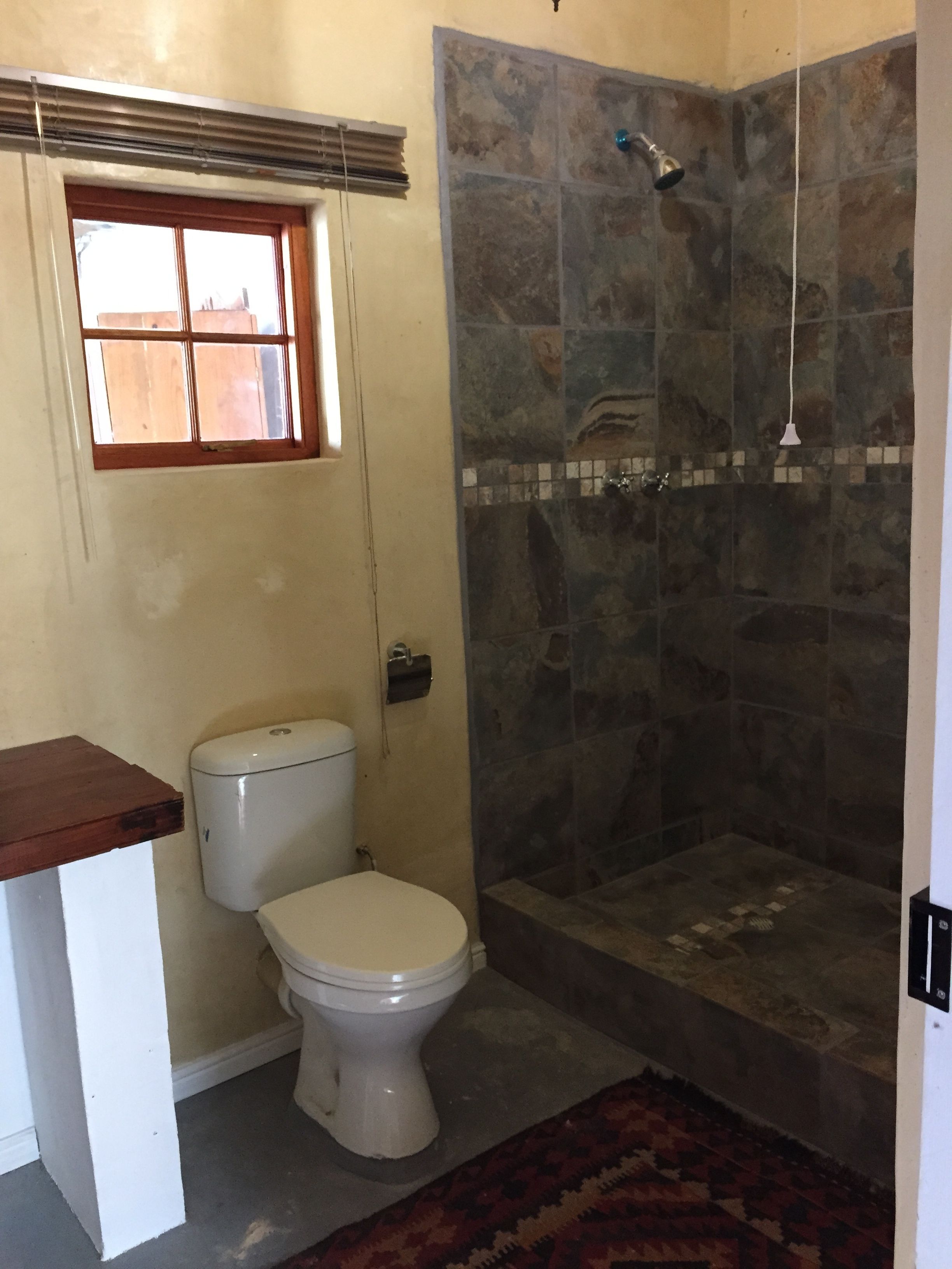 A bathroom with a toilet, a shower with stone tiles, and a small window.