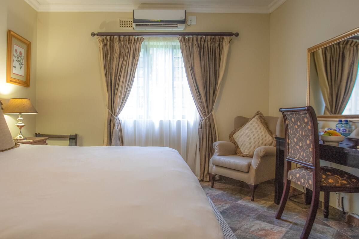 A hotel room with a large bed, a desk with a chair, a mirror, and a window with curtains.