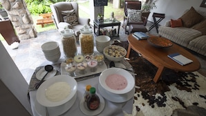 A breakfast buffet with various dishes and condiments on a table, surrounded by seating and a stone wall. - At Heritage House (St. Lucia)