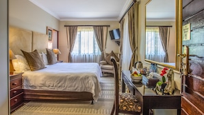 A well-lit hotel room with a large bed, a desk with a mirror, a chair, and a small table with a vase of flowers. - At Heritage House (St. Lucia)