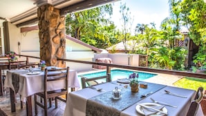 A restaurant with outdoor seating overlooking a pool, featuring stone pillars and lush greenery. - At Heritage House (St. Lucia)