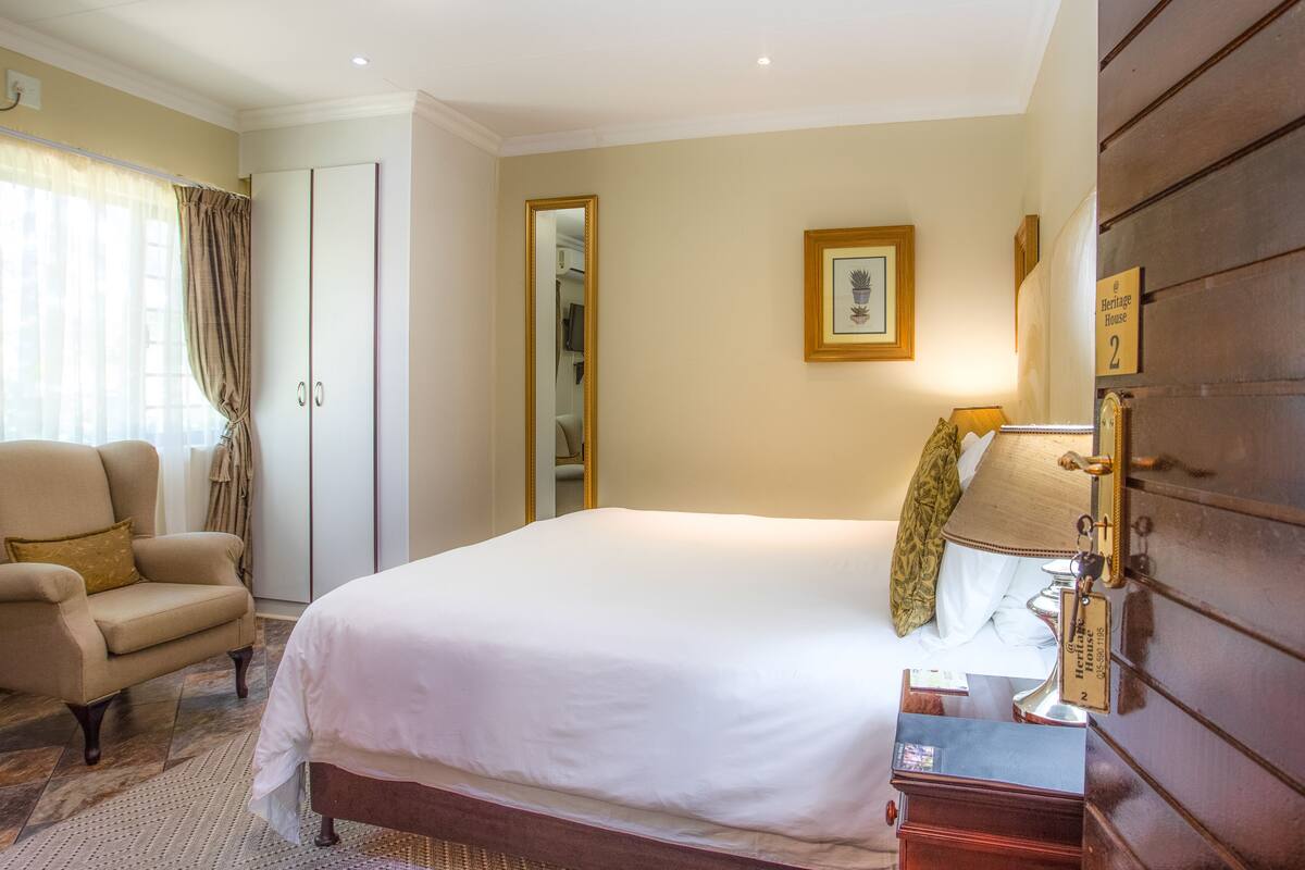 A hotel room with a large bed, a chair, a wardrobe, a mirror, and a lamp.