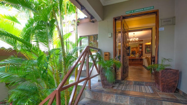 A hotel entrance with a staircase leading to a reception area, surrounded by lush greenery. - At Heritage House (St. Lucia)