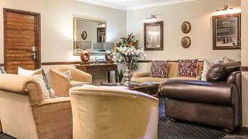 Una sala de estar bien amoblada, con un conjunto de sofá color beige, un sillón de cuero marrón, una mesa de centro y un jarrón decorativo con flores.