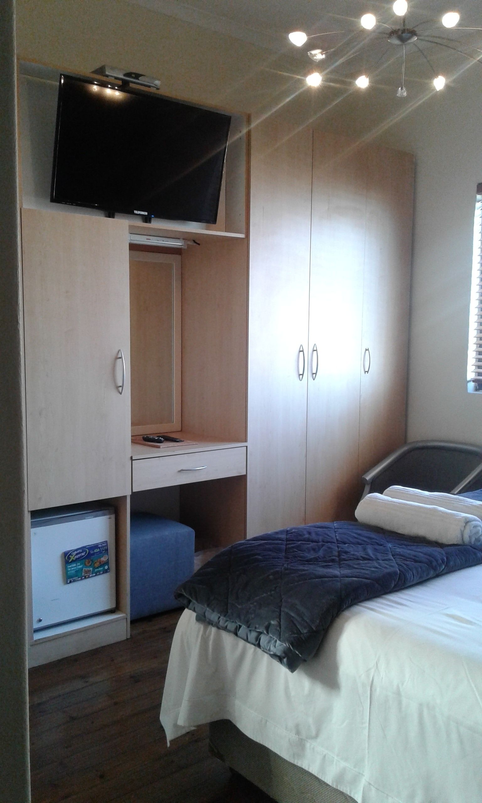 A bedroom with a bed, a TV mounted above a desk, and a wardrobe.