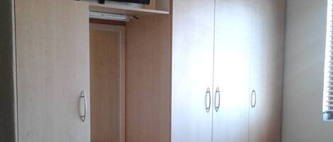 A bedroom with a bed, a TV mounted above a desk, and a wardrobe.