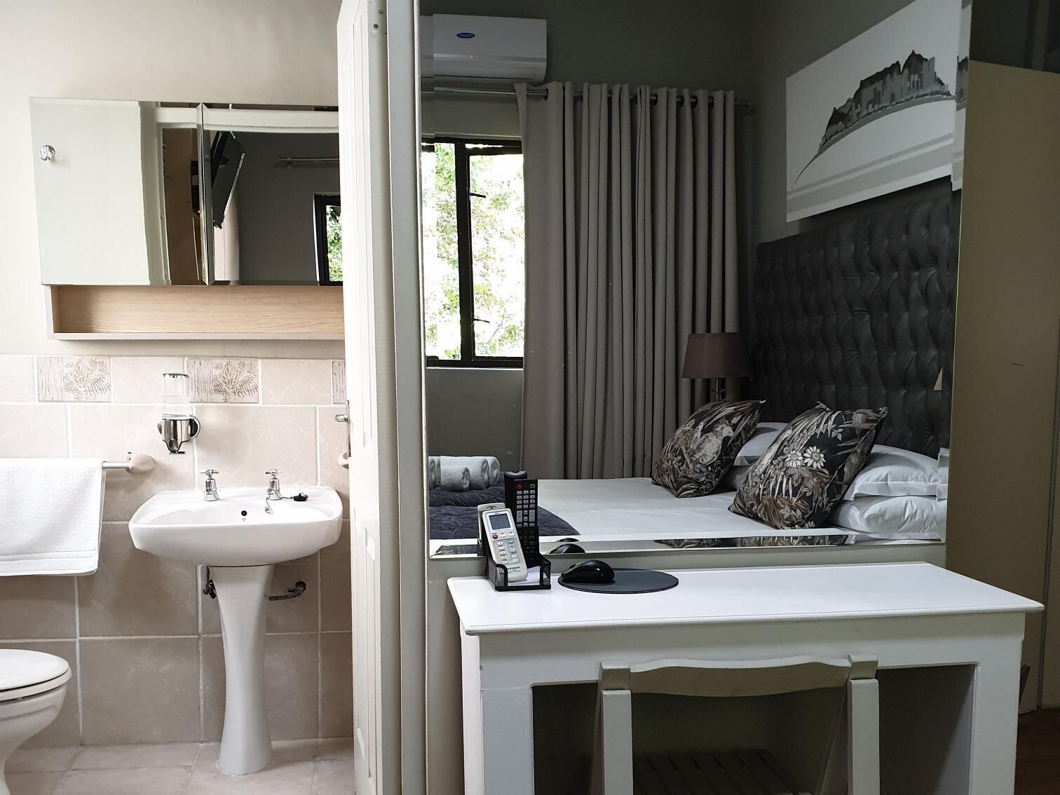 A bedroom with a bed, bedside table, and a bathroom with a sink and toilet.