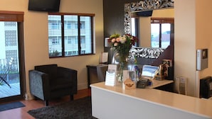A reception area with a flat-screen TV, a large mirror, a vase with flowers, a desk with a phone, and a chair. - Leeuwenzee Guest House (Cape Town)