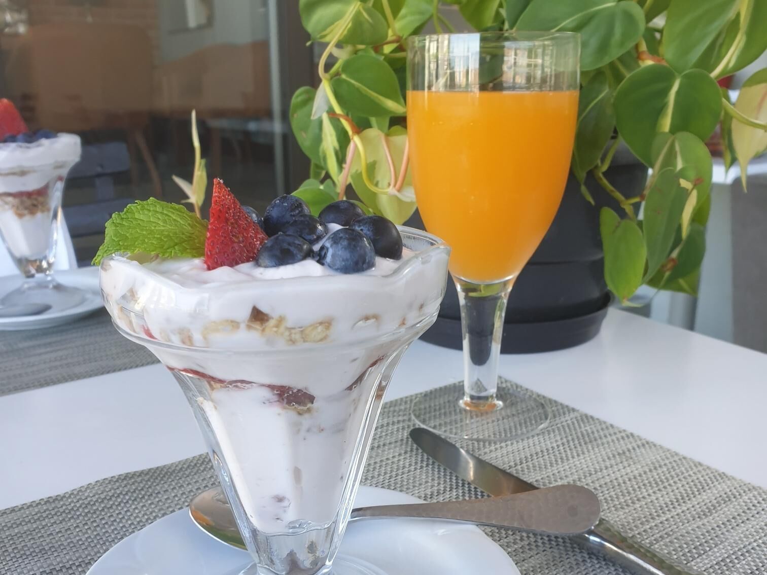 En dessert i en glasskål med jordgubbar, blåbär och ett myntablad ovanpå, bredvid ett glas apelsinjuice.