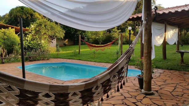 A pool area with a hammock, a pergola, and a grassy garden.