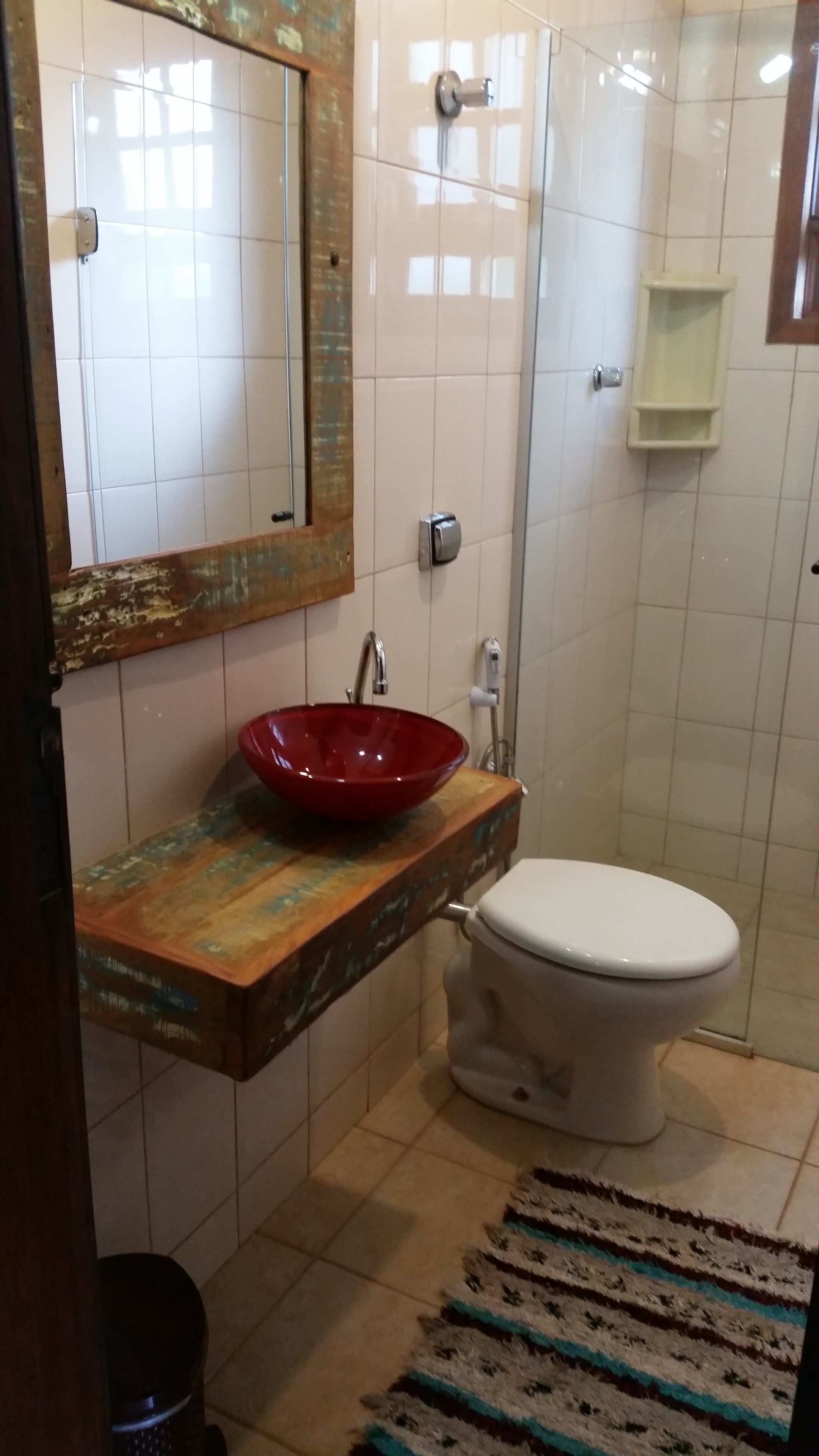 A bathroom with a red vessel sink, a white toilet, a mirror, and a shower area.